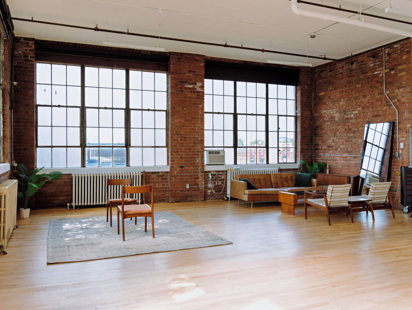 Wide view of the empty brick loft with tall factory windows, hardwood floors and a seating area