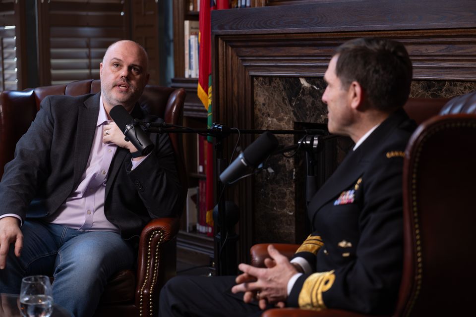 Two men talking in a library with a Canadian flag behind them